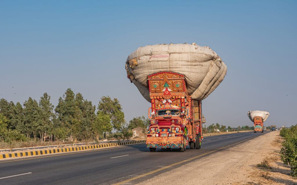 Sebuah truk Pakistan berwarna merah cerah yang dihias, bergerak di jalanan sebagai representasi seni Truck Art yang hidup