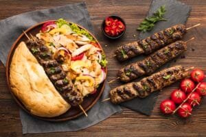 Beberapa tusuk seekh kebab daging cincang yang dipanggang, disajikan di piring dengan roti naan, salad, dan irisan cabai merah.